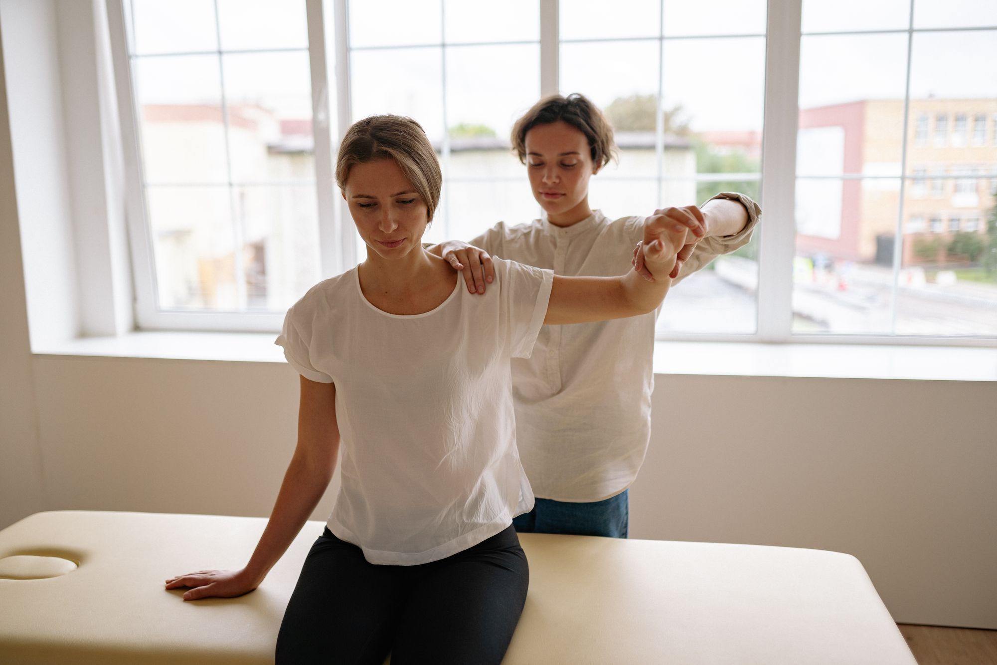 A physical therapist guiding a patient through a shoulder stretch in a bright treatment room
